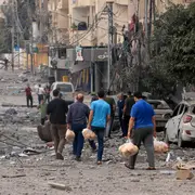 Hombres palestinos llevan pan a través de una calle fuertemente bombardeada después de los ataques aéreos israelíes en la ciudad de Gaza el 10 de octubre de 2023.