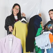 Dos chicas sosteniendo perchas con ropa.