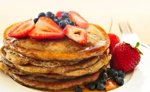 Un plato de pancakes con miel, frutillas y arándanos