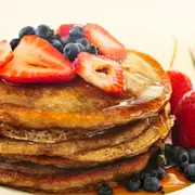 Un plato de pancakes con miel, frutillas y arándanos