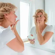 Una mujer mirándose al espejo mientras se aplica una crema