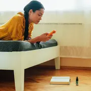 Mujer tirada en la cama mirando el teléfono celular