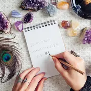 Mujer anotando números en un anotador, rodeada de cristales.