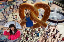 Fotograma de "Crazy ex-girlfriend", con una mujer apoyada en un pretzel gigante y debajo de ella, un cuerpo de bailarines.