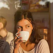Un mujer tomando una taza de café mirando por la ventana