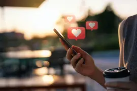 Una mano sosteniendo un celular del que salen corazones.