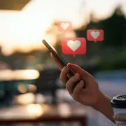 Una mano sosteniendo un celular del que salen corazones.