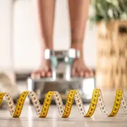 Los pies de una mujer sobre una balaza y un centímetro en primer plano.