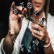 Una mano cortando un mechón de pelo y encima, la rueda zodiacal con los símbolos de los 12 signos del Zodíaco.