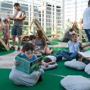 Niños leyendo libros en un parque con libros gigantes en el centro cultural de la ciencia