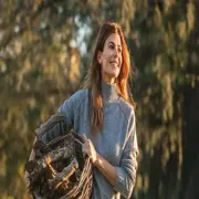 Juliana Awada lleva un sueter gris y un canasto con troncos de madera en el campo