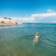 Fotografía de una chica nadando en un mar cristalino y de lejos se ve la arena blanca con un par de personas