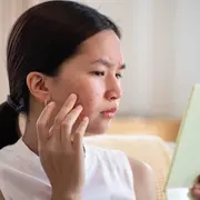 Una mujer mirándose al espejo mientras se aplica una crema