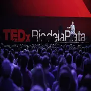 Una mujer adulta dando una charla frente a un teatro lleno de gente y atrás se ve le logo de TEDxRiodelaPlata