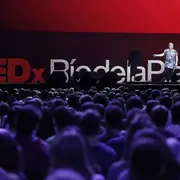 Una mujer adulta dando una charla frente a un teatro lleno de gente y atrás se ve le logo de TEDxRiodelaPlata