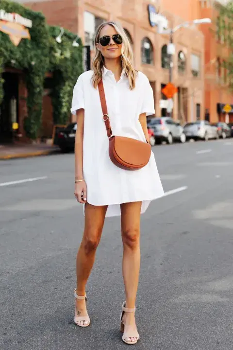 Vestido blanco camisero con sandalias altas y bandolera en tonos neutros. Vestido blanco camisero con sandalias altas y bandolera en tonos neutros.