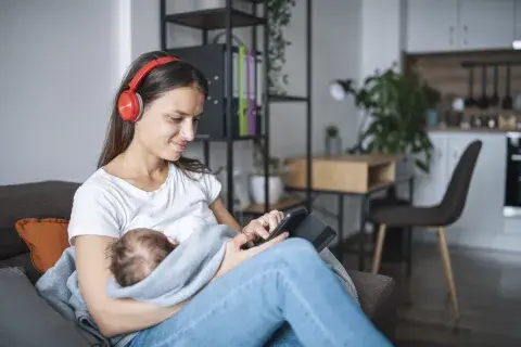 Mujer amamantando y escuchando un podcast. Mujer amamantando y escuchando un podcast.