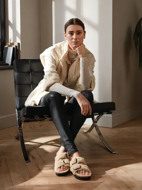 Look confy de una chica sentada en una silla con pantalón negro, sandalias de peluche y una camisa blanca Look confy de una chica sentada en una silla con pantalón negro, sandalias de peluche y una camisa blanca