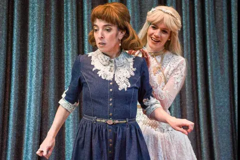 Dos mujeres en el escenario; una le toca el pelo a la otra. Dos mujeres en el escenario; una le toca el pelo a la otra.