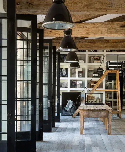 El salón principal es amplio y luminoso, con muros de ladrillo pintado de blanco, sofás oscuros que dialogan con tonos claros, y una chimenea decorativa como punto focal