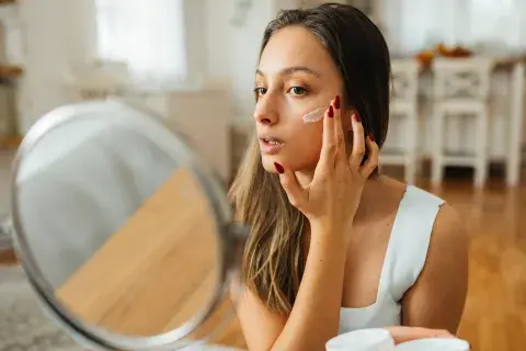 Foto de mujer frente al espejo aplicándose crema en la cara. Foto de mujer frente al espejo aplicándose crema en la cara.