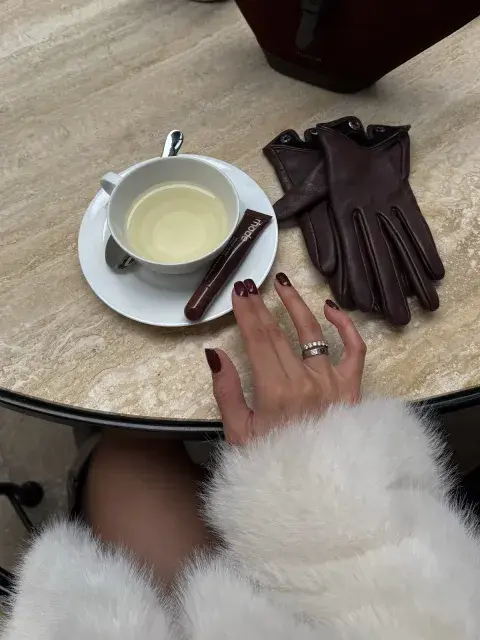 Una mujer tomando café con guantes de cuero apoyados en la mesa Una mujer tomando café con guantes de cuero apoyados en la mesa