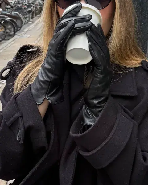 Una mujer tomando un café con sus manos con guantes de cuero negro Una mujer tomando un café con sus manos con guantes de cuero negro
