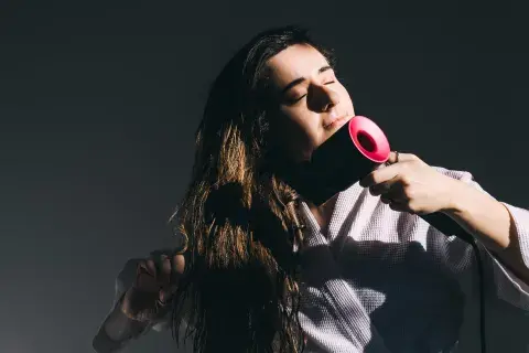 Una mujer secándose el pelo con un secador de color negro y rosa