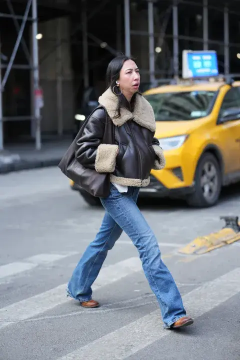 Una mujer con campera de corderito en color marron cruzando una calle de nueva york Una mujer con campera de corderito en color marron cruzando una calle de nueva york