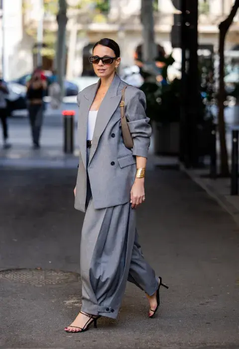 Un mujer usando un conjunto oversize en color gris claro con stilettos y una cartera 