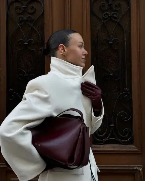 Una mujer con un abrigo en color blanco y accesorios en color borgoña