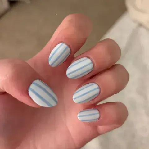La mano de una mujer con uñas rayadas en celeste y blanco
