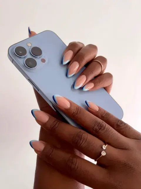 Una mujer sosteniendo un teléfono celular con las uñas francesita en color azul y blanco
