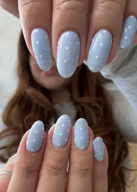 Una mujer con las uñas a lunares celestes y blancos