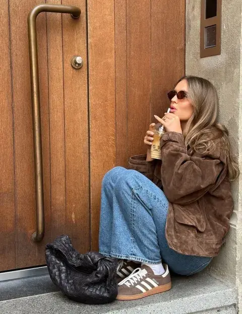 Una mujer en el umbral de una casa mostrando sus zapatillas en color camel Una mujer en el umbral de una casa mostrando sus zapatillas en color camel