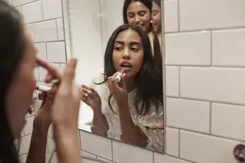 Tres mujeres frente al espejo pintándose los labios