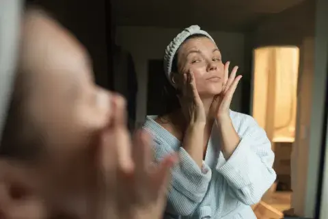 una mujer mirándose al espejo poniendose crema en la cara una mujer mirándose al espejo poniendose crema en la cara