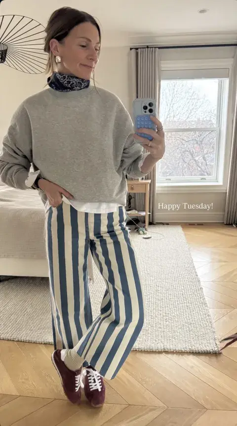 Una mujer frente a un espejo sacandose una foto con pantalon a rayas Una mujer frente a un espejo sacandose una foto con pantalon a rayas