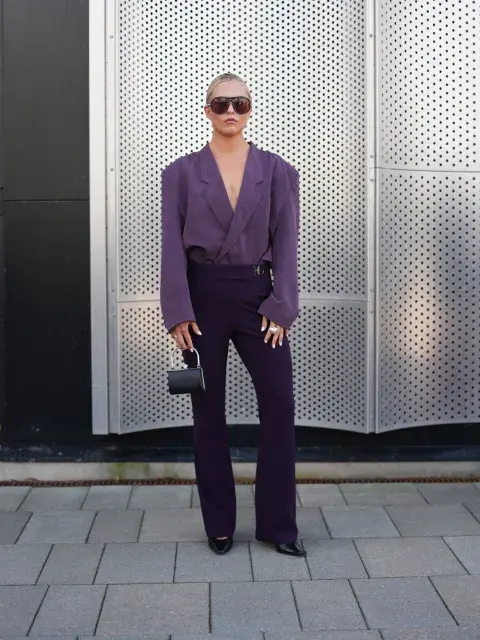 Una mujer parada en la calle con un look en color violeta y lentes de sol Una mujer parada en la calle con un look en color violeta y lentes de sol