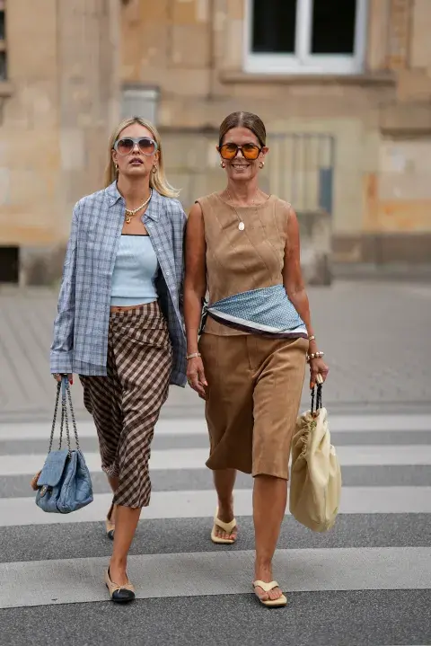 Dos mujeres cruzando la calle con looks en color celeste y tonos tierra y lentes XL Dos mujeres cruzando la calle con looks en color celeste y tonos tierra y lentes XL