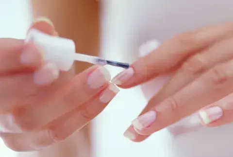 Una mujer pintándose las uñas con base