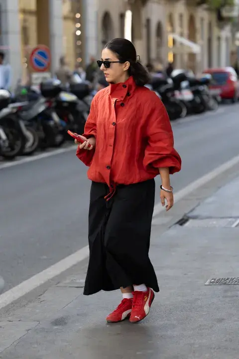 Una mujer caminando por la calle con zapatillas puma en color rojo y una chaqueta combinada