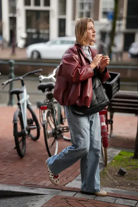 Una mujer en Amsterdam fashion week con un look de street style con una campera de cuero en color borgoña