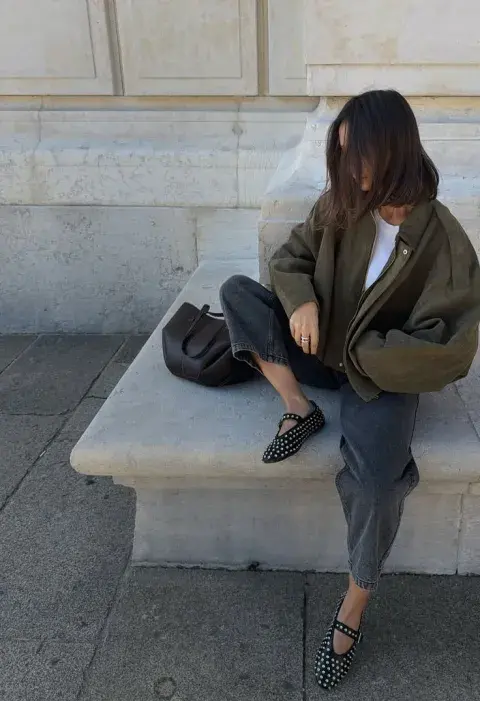 Una mujer con ballerinas con tachas, campera verde y un pantalón de vestir en color gris Una mujer con ballerinas con tachas, campera verde y un pantalón de vestir en color gris