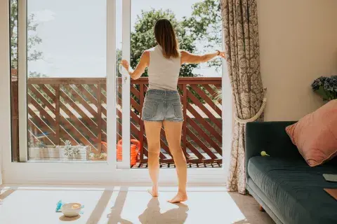 Mujer abriendo la ventana de un balcón en su departamento.