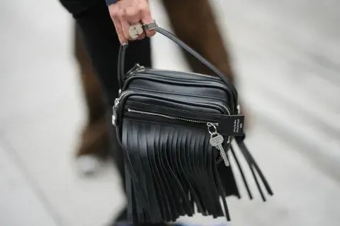 Una mujer caminando en paris fashion week con una cartera con flecos