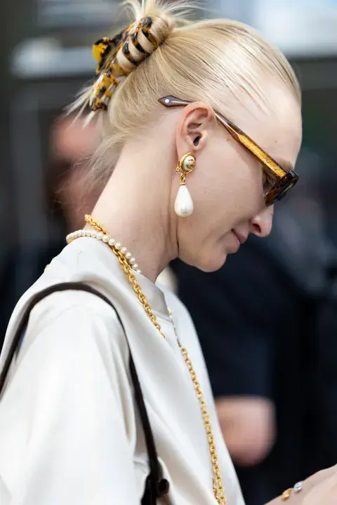 Una mujer caminando por parís fashion week con accesorios en color dorado
