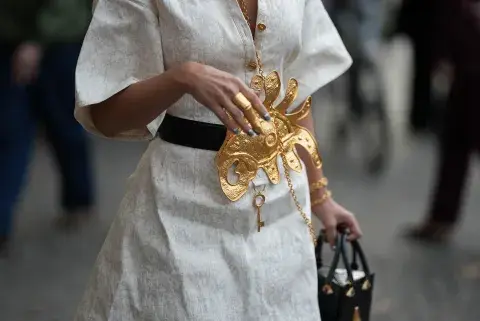 Una mujer caminando por parís fashion week con accesorios en color dorado