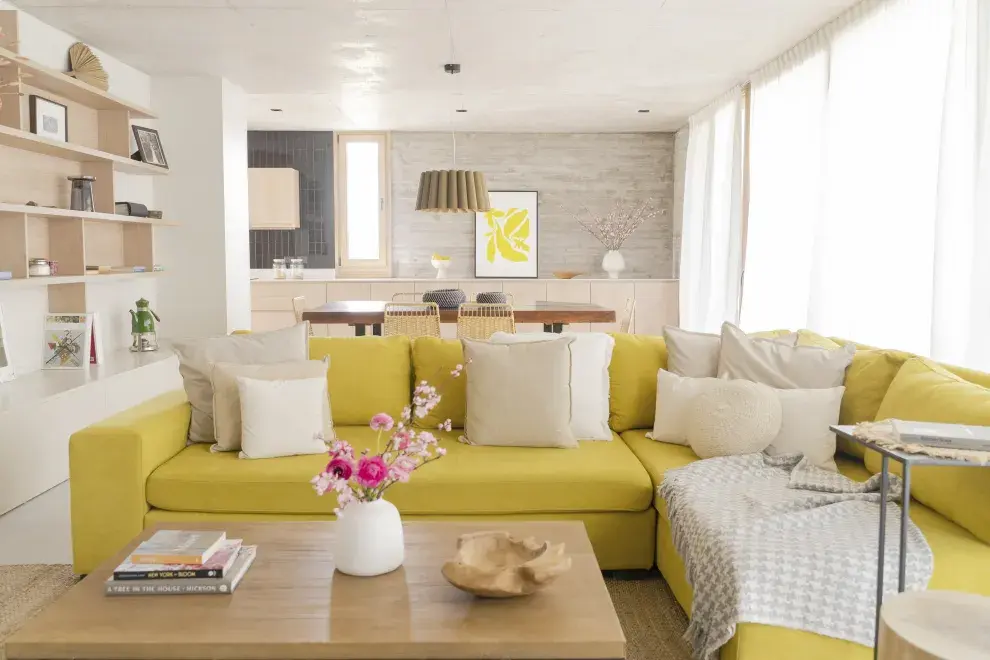 En el living, el sillón amarillo es protagonista. Almohadones, centro de mesa, jarrón y manta conjugan materiales nobles y tonos tierra (todos de @salazarcasa). Arreglo floral (@blomsterflower).