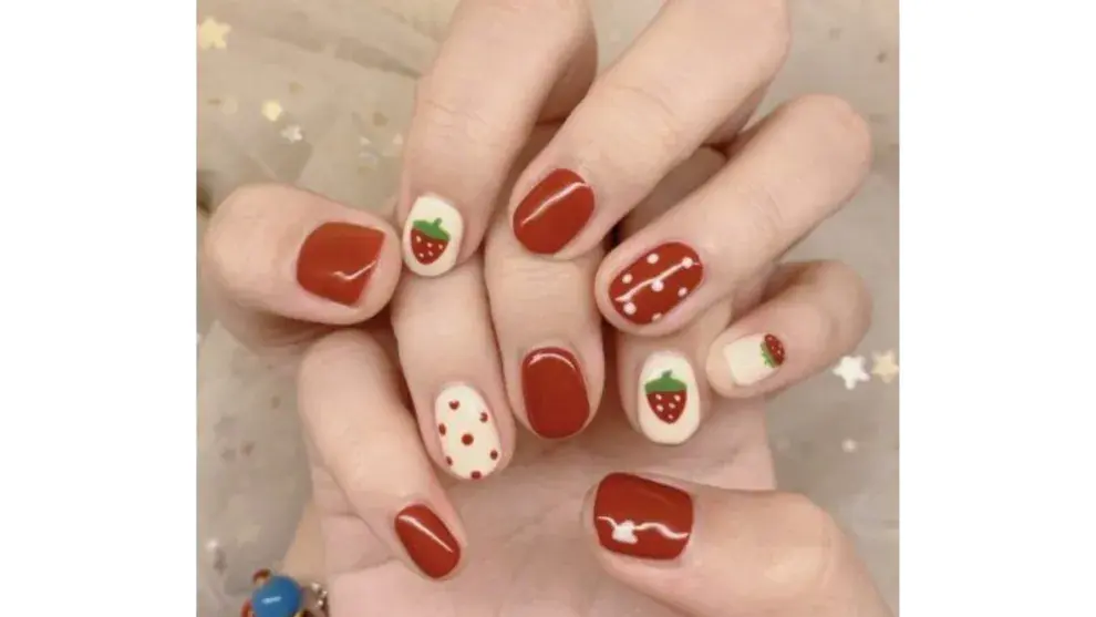 Nail art con uñas en color rojo con pintitas blancas y frutillas